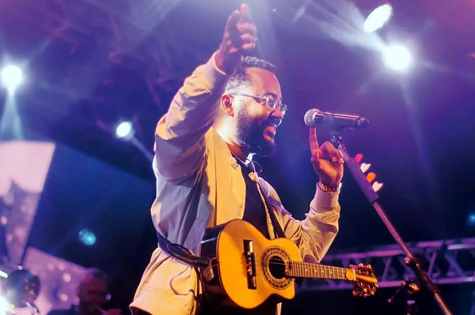 Cantor com violão e microfone em show do festival, sob luzes roxas